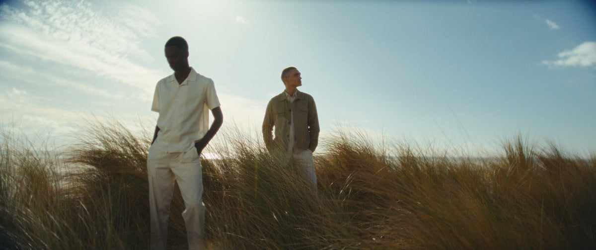 Two models wearing Ogun among coastal grasses.